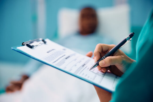 Close up of female doctor writing medical data while visiting her patient in hospital ward.