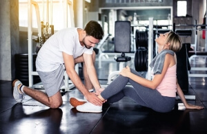 Man helps woman with injured ankle in gym