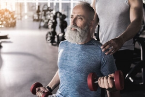 Older man training his biceps in gym with instructor