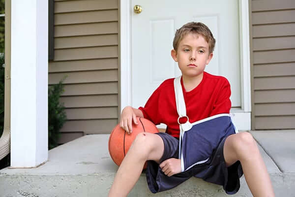 Boy with arm in a sling sitting with a basketball